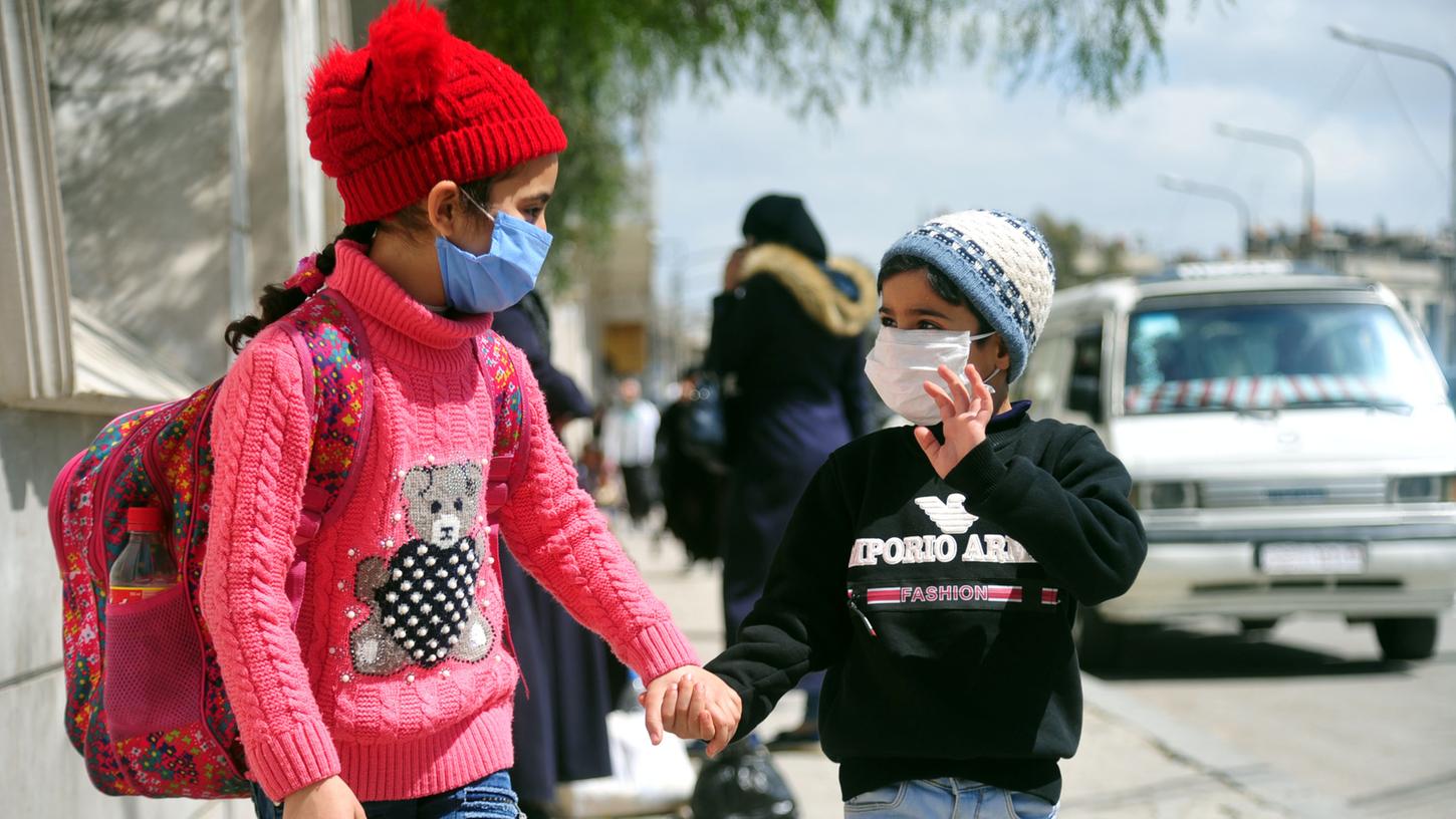 Zwei Kinder in Damaskus sind aufgrund der Corona-Pandemie mit Mundschutzmasken draußen unterwegs.
