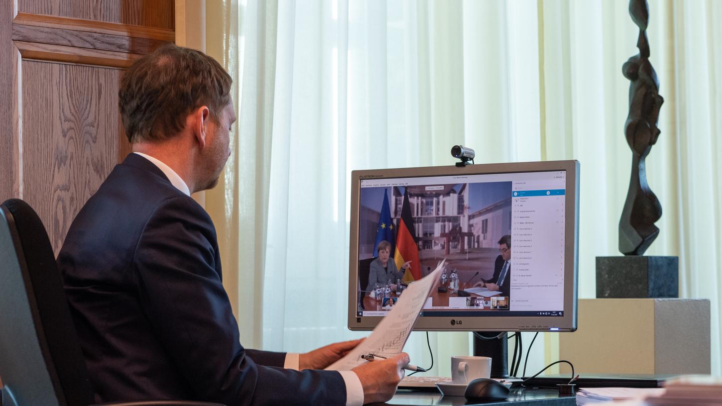 Michael Kretschmer (CDU), Ministerpräsident von Sachsen, sitzt in einem Büro in der Staatskanzlei vor einem Computerbildschirm und spricht während einer Schaltkonferenz per Video mit Bundeskanzlerin Angela Merkel (CDU, l.) und Markus Söder (CSU), Ministerpräsident von Bayern.