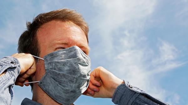 So ist es richtig: Zuerst müssen die Haare aus dem Gesicht genommen werden, Bärte werden am besten mindestens soweit rasiert, dass sie unter der Maske verschwinden. Nur mit gründlich gereinigten Händen sollte sie angelegt werden. Zuerst zieht man die Bänder hinter das Ohr, berührt den Stoff nur außen und drückt den Nasenbügel fest, damit keine Löcher entstehen. Am besten wird die Maske bis unter das Kinn gezogen.