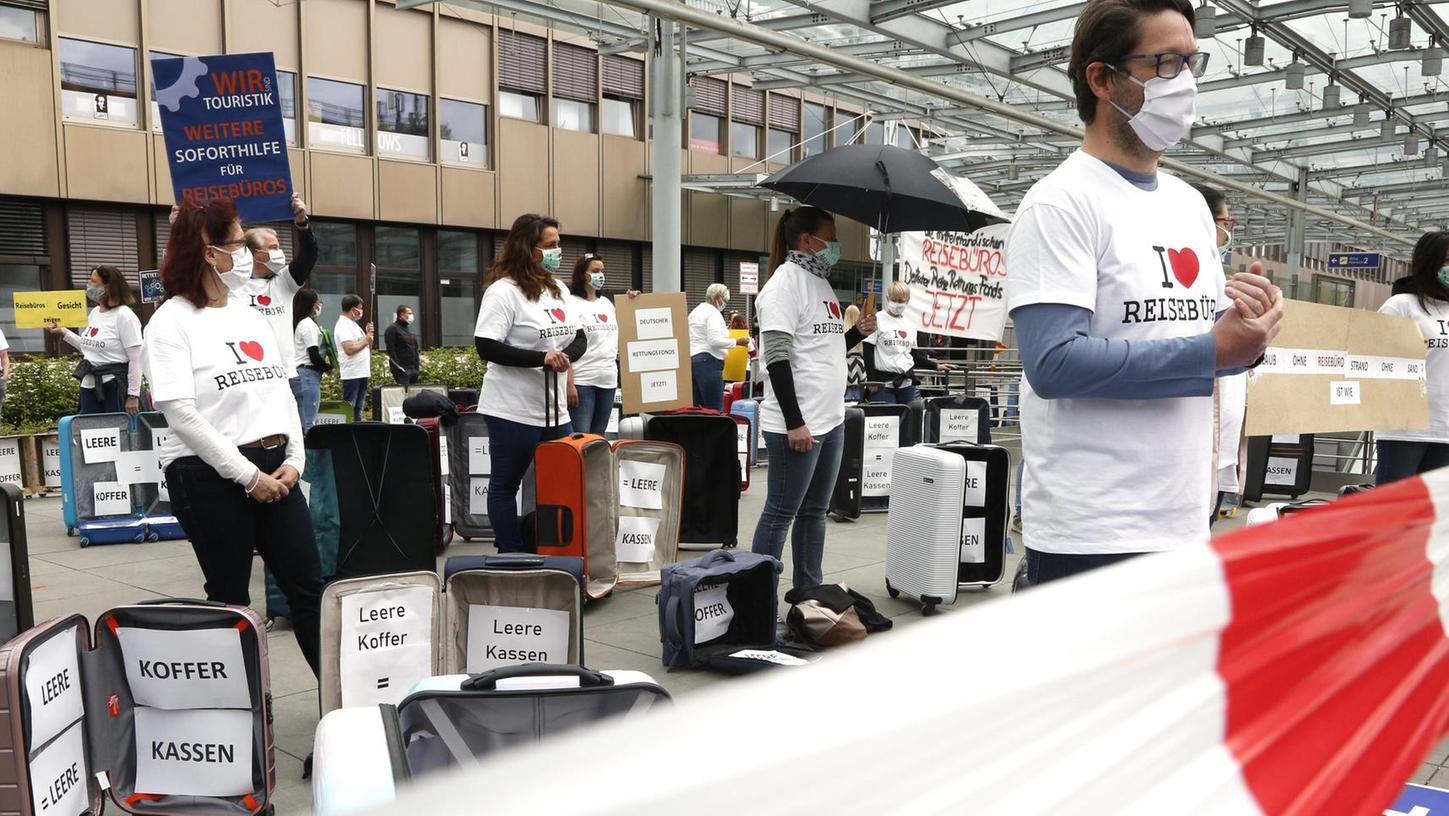 Die Mitarbeiter der Reisebranche zeigen mit Koffern, beschrifteten Masken, Shirts und Schildern Gesicht und bekennen sich mit einem roten Herz zum Reisebüro.