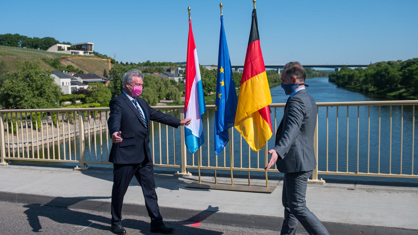Der luxemburger Außenminister Jean Asselborn (l) und Bundesaußenminister Heiko Maas (SPD) treffen sich auf der Brücke über die Mosel, die das saarländische Perl und das Luxemburger Schengen verbindet. In der Nacht wurden die Grenzen zwischen Deutschland und Luxemburg wieder geöffnet, die zuvor wegen der Bekämpfung des Coronavirus geschlossen wurde.