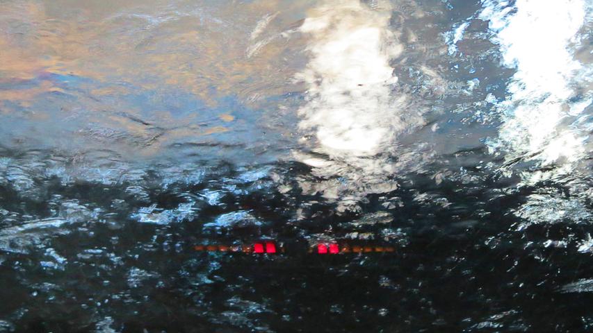 In einer Autowaschstraße von innen gegen die Windschutzscheibe fotografiert: Während das Wasser über die Glasfläche läuft, lassen die rotierenden Waschwalzen die Abstandswarnlampen auf dem Armaturenbrett und im Rückspiegel aufleuchten. So mutiert die Waschanlage fast zur Geisterbahn.