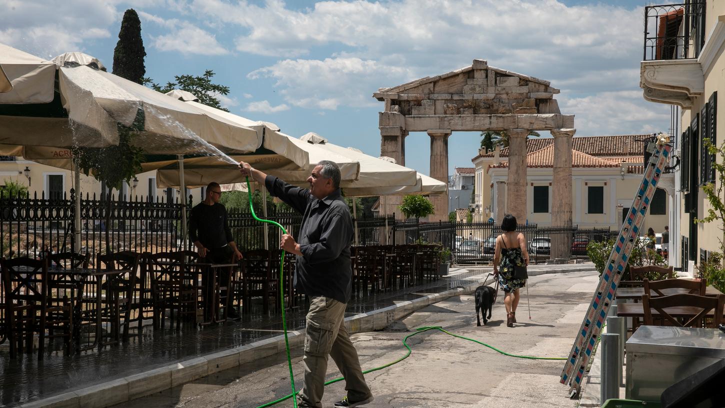 Athen: Ein Mann reinigt Sonnenschirme vor einer Taverne im Plaka-Viertel mit Wasser aus einem Schlauch. Restaurants und Cafés dürfen in Griechenland nach der Corona-Zwangspause am 25. Mai wieder öffnen.