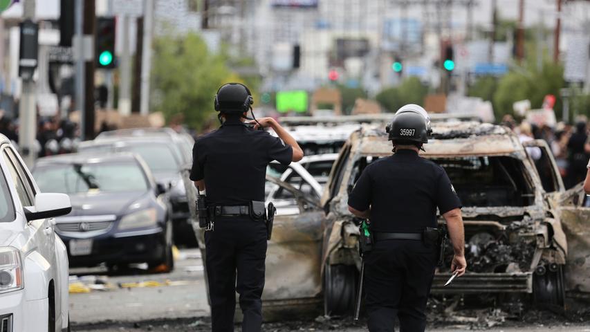 30.05.2020, USA, Los Angeles: Polizisten gehen während eines Protestes auf einer Straße, auf der verbrannte Autos stehen. Der Protest richtet sich nach dem gewaltsamen Tod des Afroamerikaners Floyd durch einen weißen Polizisten gegen Rassismus und Polizeigewalt. Die teils schweren Ausschreitungen in verschiedenen US-Metropolen dauern seit mehreren Tagen an. Foto: -/XinHua/dpa +++ dpa-Bildfunk +++