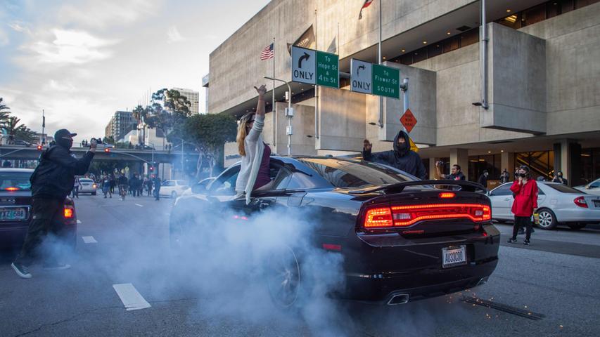 A driver burns-out tire while a passenger seats on the window gesticulating to the Police in Downtown Los Angeles on May 30, 2020 during a protest against the death of George Floyd, an unarmed black man who died while while being arrested and pinned to the ground by the knee of a Minneapolis police officer. - Clashes broke out and major cities imposed curfews as America began another night of unrest Saturday with angry demonstrators ignoring warnings from President Donald Trump that his government would stop violent protests over police brutality "cold." (Photo by Apu GOMES / AFP)
