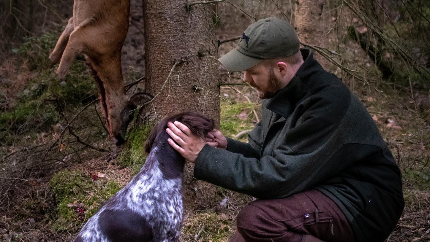 Fabian Grimm, 32, mit seinem Jagdhund Akira. Im Hintergrund hängt ein erlegtes Reh. Grimm nimmt noch im Wald die Tiere aus, bevor sie in einer Kühlkammer weiterverarbeitet werden. 