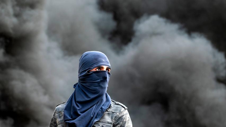 Ein vermummter Palästinenser steht während einer Demonstration vor dunklen Rauchschwaden. Zuvor war ein 29-jähriger Landsmann von ihm beerdigt worden, der von israelischen Soldaten erschossen worden war. Die genauen Umstände der Vorfalls sind ungeklärt.