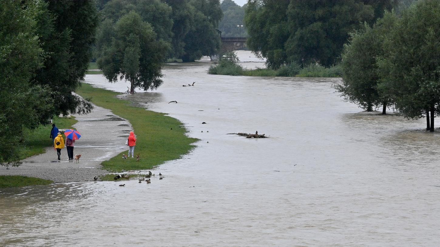 Passanten gehen nach Regenfällen am überschwemmten Ufer der Isar entlang.