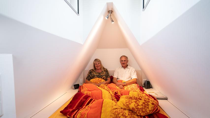Simone Stiefel und Achim Schollenberger sitzen gemeinsam im Bett im Dachgeschoss ihres kleinen Wohnhaus. Das Bett nimmt die gesamte Fläche der Etage ein.
