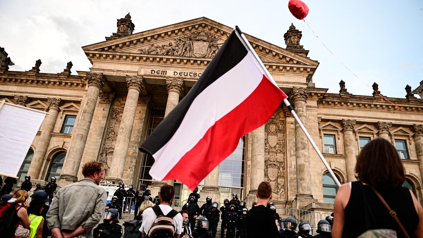 Teilnehmer einer Kundgebung gegen die Corona-Maßnahmen stehen vor dem Reichstag, einer hält eine Reichsflagge mit schwarz-weiß-roten Querstreifen.