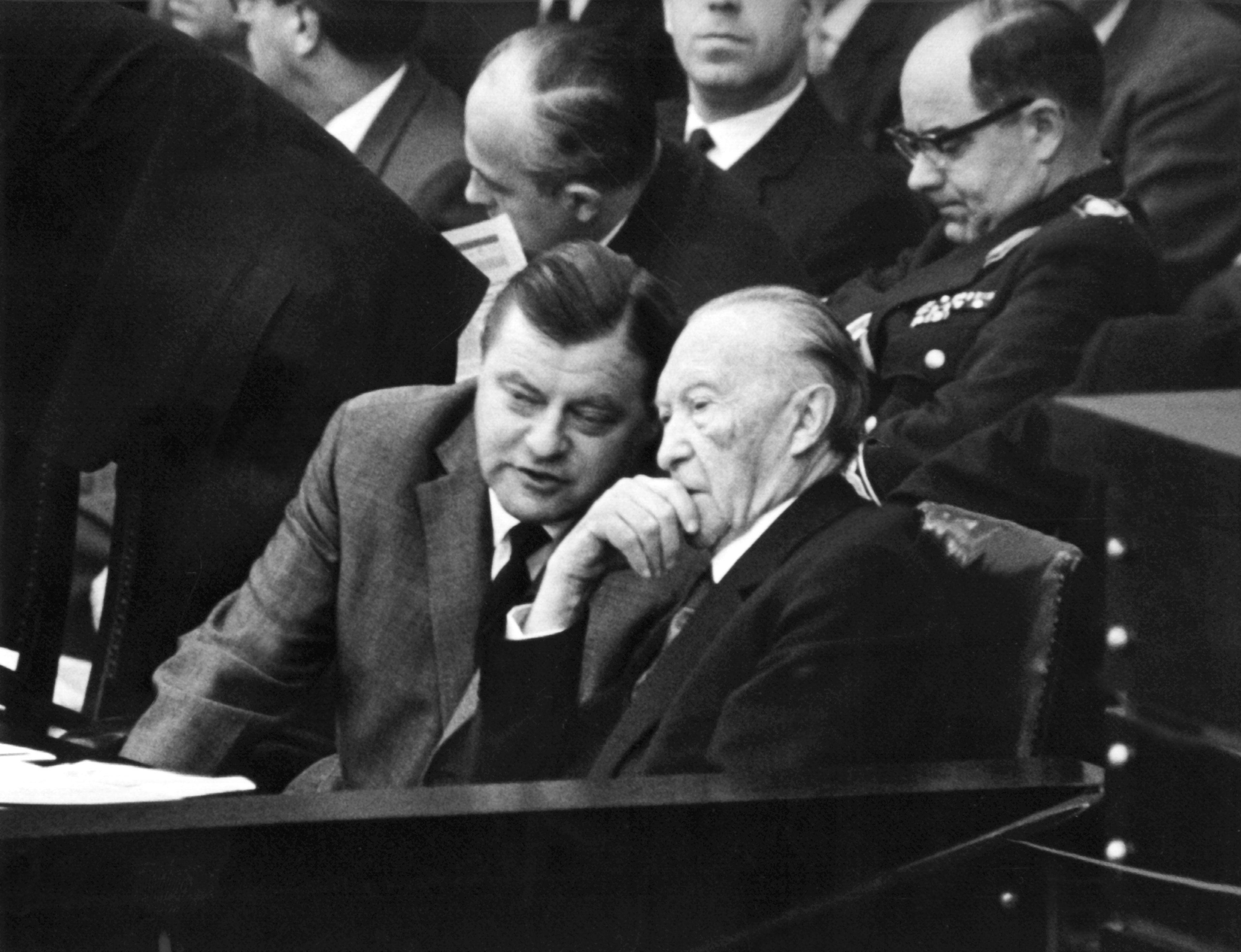Bundesverteidigungsminister Franz Josef Strauß (links) unterhält sich im Bundestag mit Bundeskanzler Konrad Adenauer (CDU) während der dritten Spiegel-Debatte im November 1962. Im Spiegel erschien der Artikel "Bedingt abwehrbereit" von Conrad Ahlers, Strauß ordnete Ermittlungen an. Die Verlagsräume der "Spiegel"-Redaktionen in Hamburg und Bonn wurden durchsucht, "Spiegel"-Herausgeber Rudolf Augstein und Chefredakteur Claus Jacobi wegen Landesverrats verhaftet. Anfangs wurde Strauß in der Spiegel-Affäre noch von Adenauer gedeckt; nach dem geschlossenen Rücktritt der FDP-Minister am 19. November 1962 war Strauß am 30. November 1962 gezwungen, von seinem Amt als Verteidigungsminister zurückzutreten. Adenauer bildete am 14. Dezember 1962 ein neues Kabinett mit der FDP und ohne Strauß.