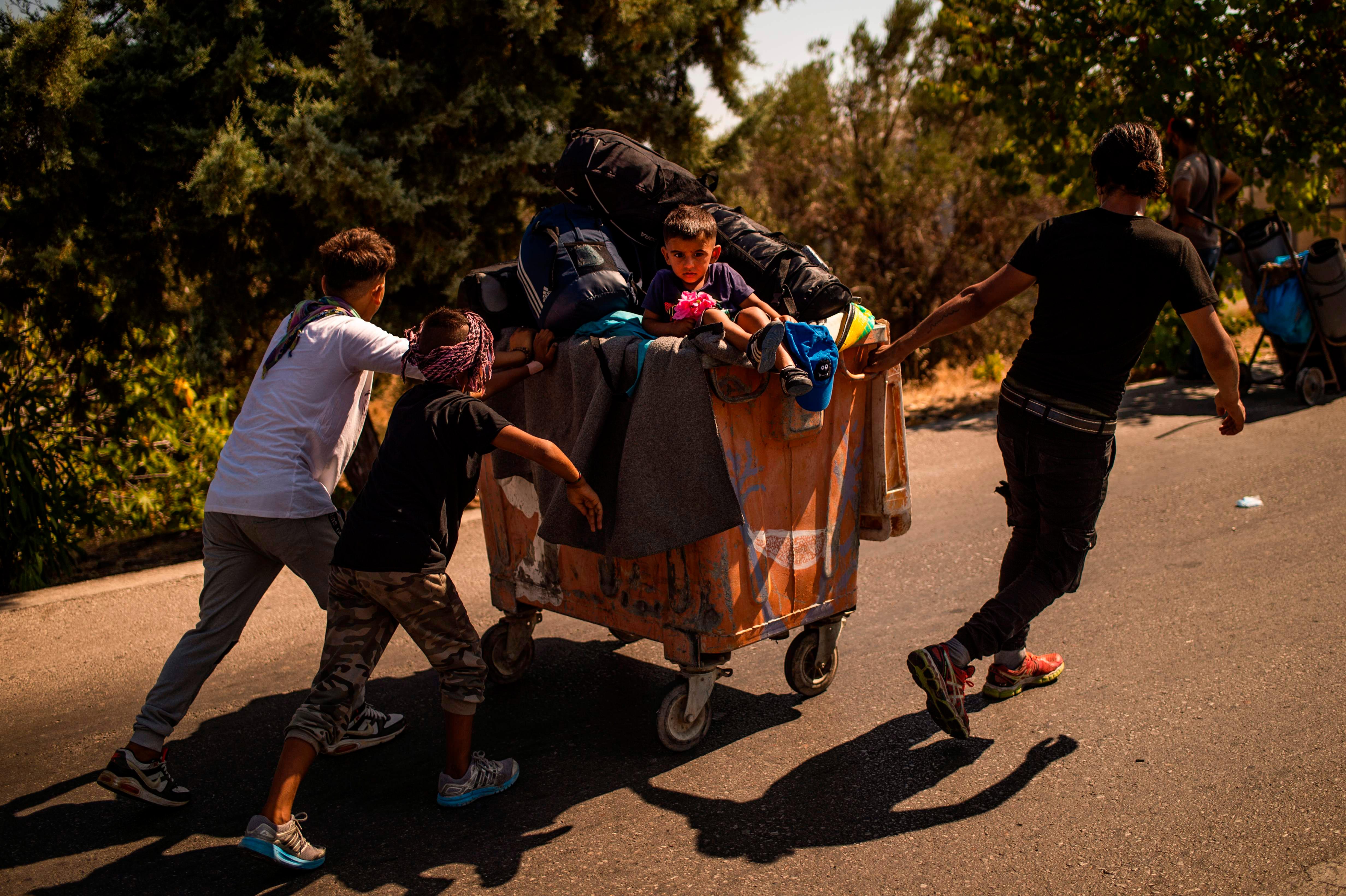 In großen Roll-Containern stapelt sich das Hab und Gut der Geflüchteten - mittendrin ein kleiner Junge der von anderen jungen Migranten über die Straße gezogen wird.