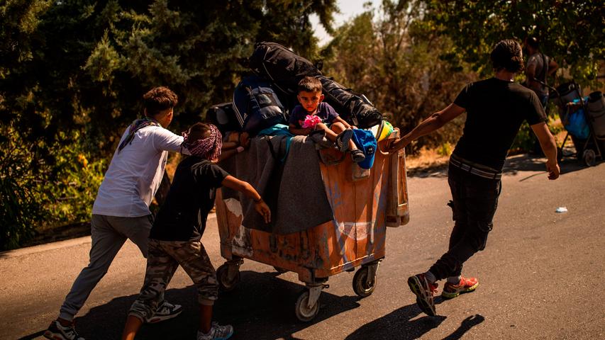 In großen Roll-Containern stapelt sich das Hab und Gut der Geflüchteten - mittendrin ein kleiner Junge der von anderen jungen Migranten über die Straße gezogen wird.