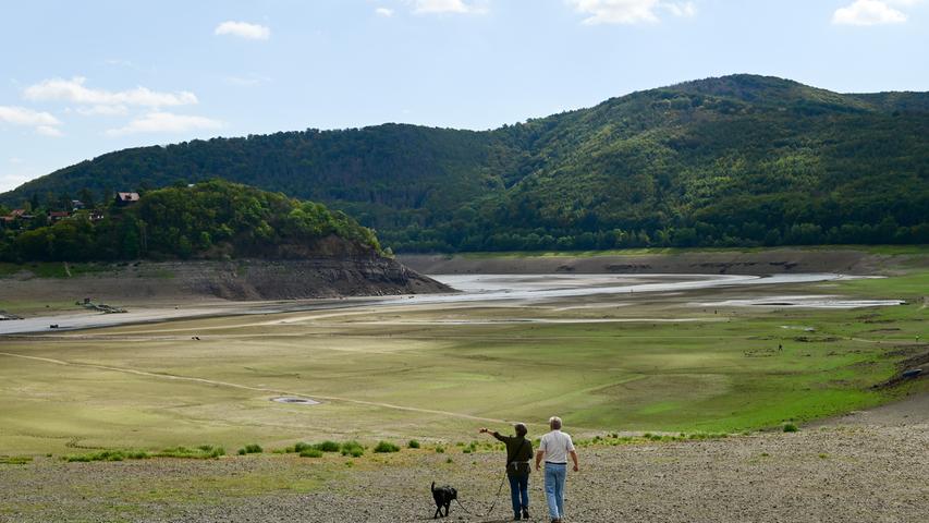 Zwei Menschen stehen mit ihrem Hund vor der Bringhäuser Bucht auf dem Grund des Edersees. Im Herbst ist der Grund des Sees bis auf den Wasserlauf des Flusses Eder (Hintergrund) in weiten Teilen begehbar. 