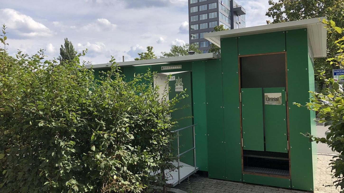 Zum Teil hinter Hecken versteckt steht das grüne Bio-Toilettenhäuschen am Rand des Parkplatzes beim Norikus am Wöhrder See.