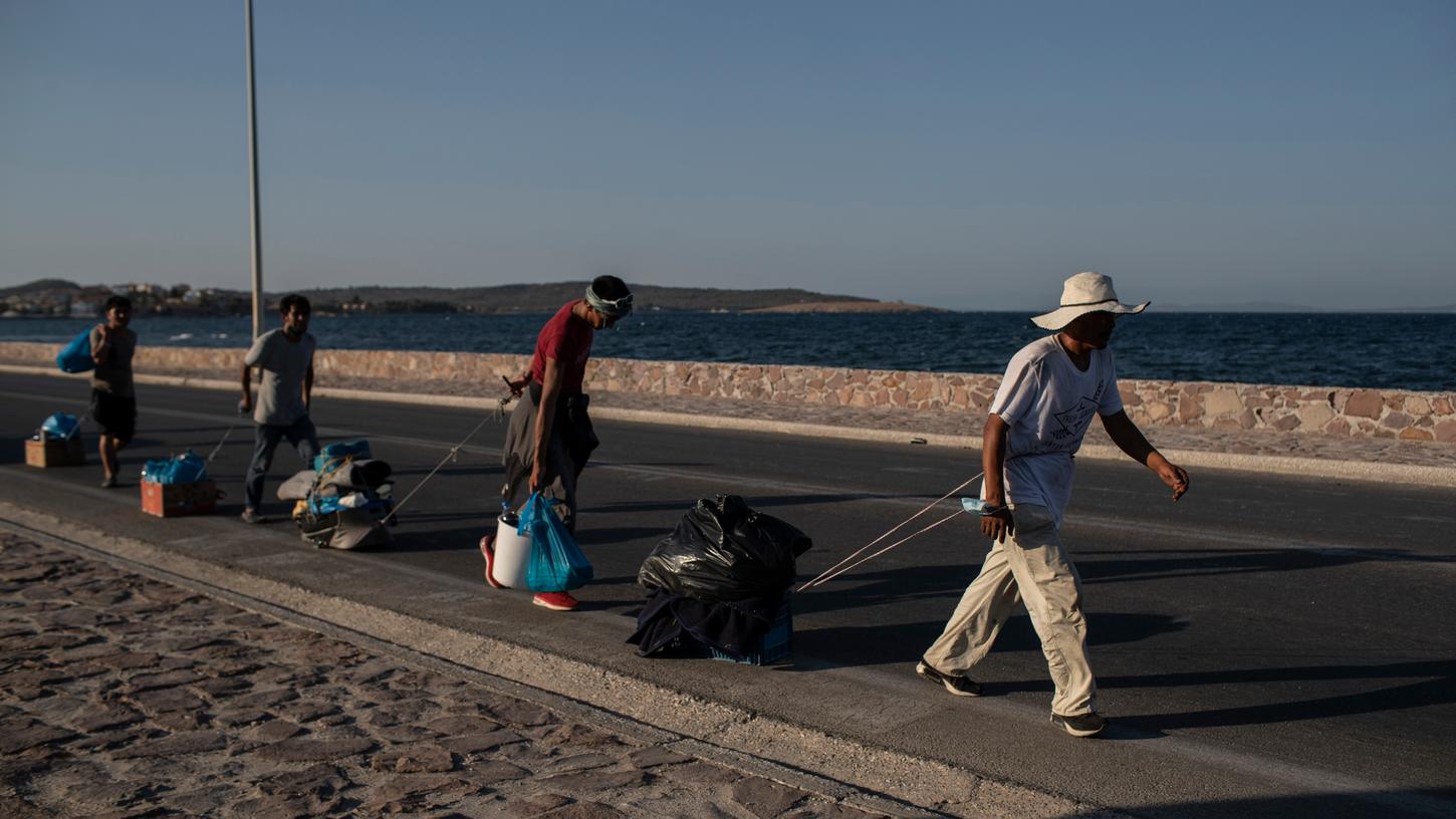 Migranten ziehen ihre Habseligkeiten mit sich und gehen entlang einer Straße in der Nähe der Stadt Mytilene auf der nordöstlichen Seite der Insel Lesbos.