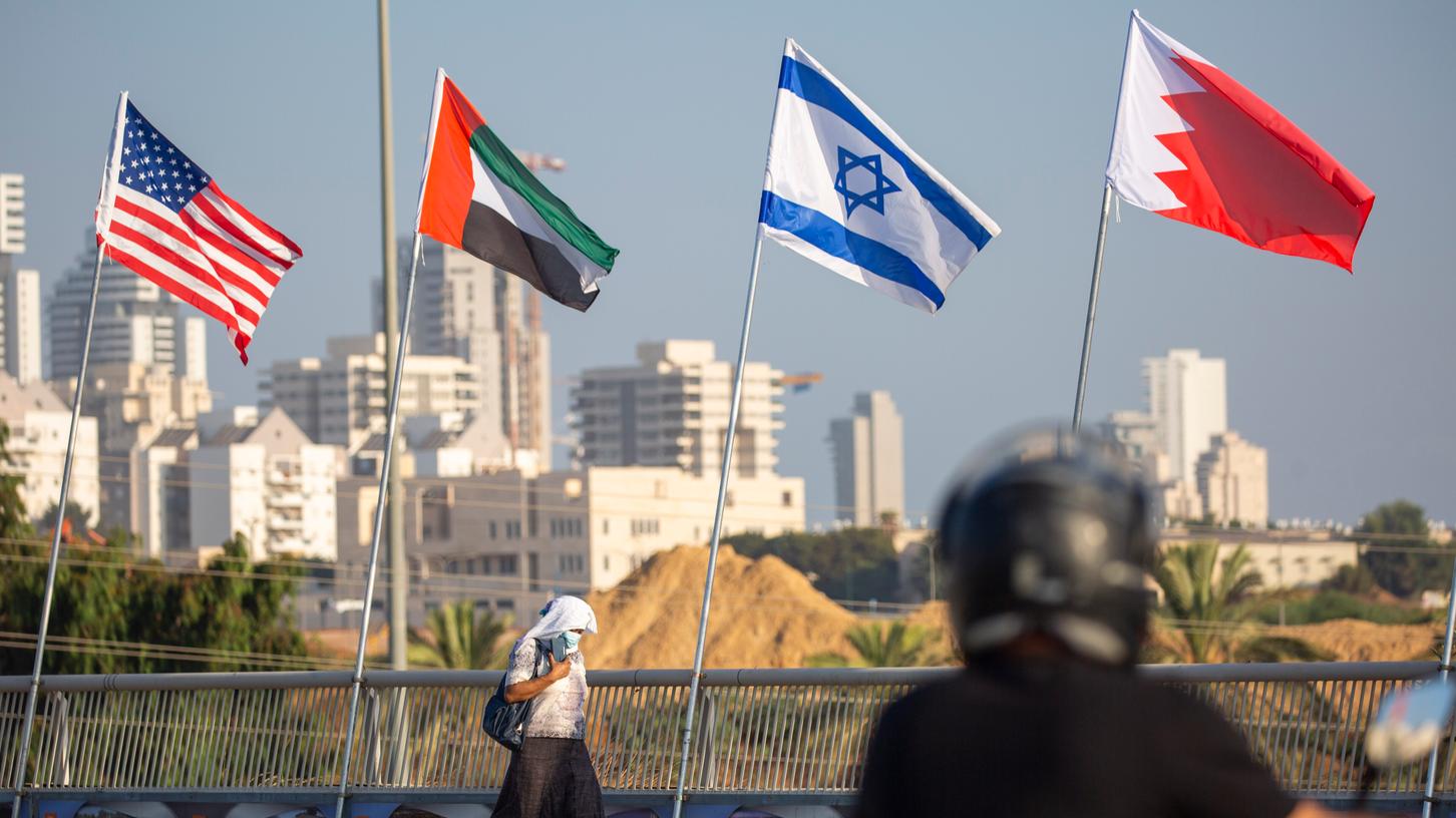 Eine Frau, die einen Mundschutz trägt, geht an den Flaggen der USA (v. li. n. re.), der Vereinigten Arabischen Emirate, Israels und Bahrains vorbei.