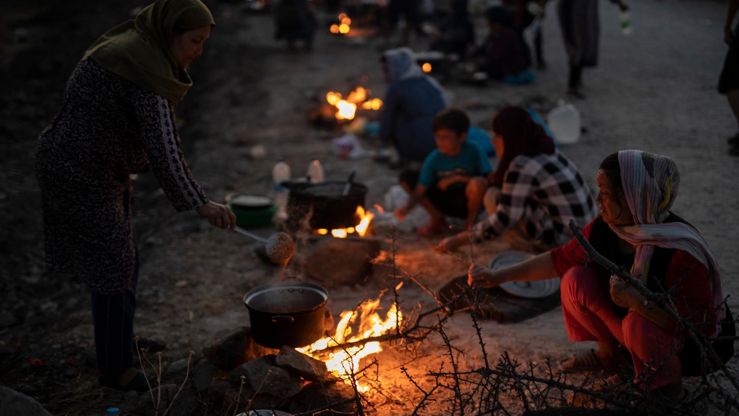 Migranten sitzen an einer Straße in der Nähe der Stadt Mytilene um kleine Feuer und bereiten Essen zu.
