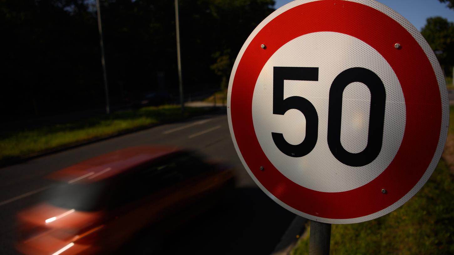 Ein Verkehrsschild zur Geschwindigkeitsbegrenzung auf Tempo 50 steht auf einer Hauptstraße während ein Auto vorbei fährt. 
