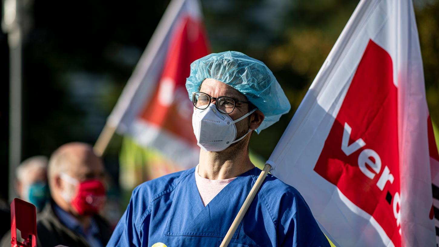 Ein Arzt mit Mund-Nasen-Schutz und OP-Haube steht vor Beginn der zweiten Runde der Tarifverhandlungen im öffentlichen Dienst von Bund und Kommunen mit einer Verdi-Flagge vor dem Kongresshotel in Potsdam.