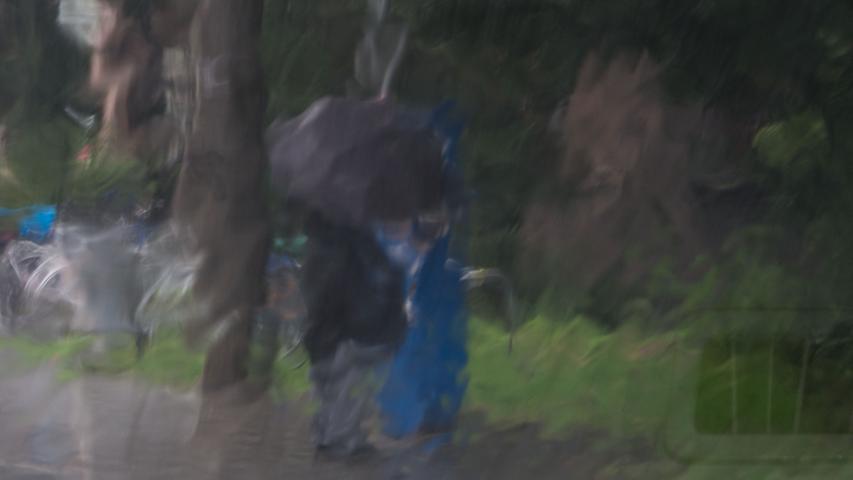 Es schüttet wie aus Kübeln, irgendwo in Nürnberg steht ein Paar und versucht sich mit einem Regenschirm zu schützen. Fotografiert durch die Windschutzscheibe eines Autos. Ein Gemälde kann kaum schöner sein.