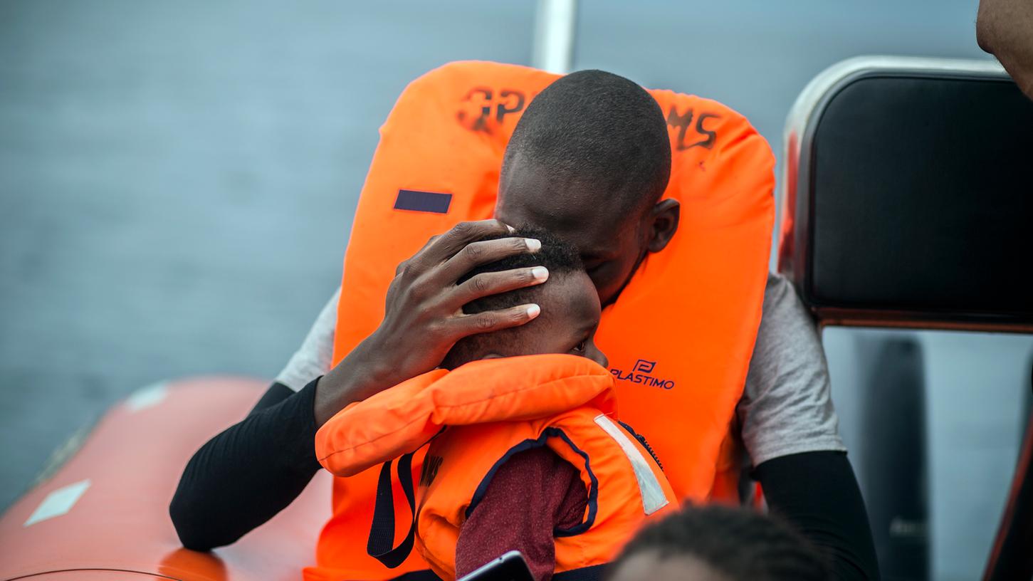 Ein Mann hält seinen Sohn im Arm, nachdem er gemeinsam mit anderen Flüchtlingen im Mittelmeer von Aktivisten gerettet wurde. Solche Hilfen hat der Nürnberger Pfarrer deutlich in Frage gestellt. 
