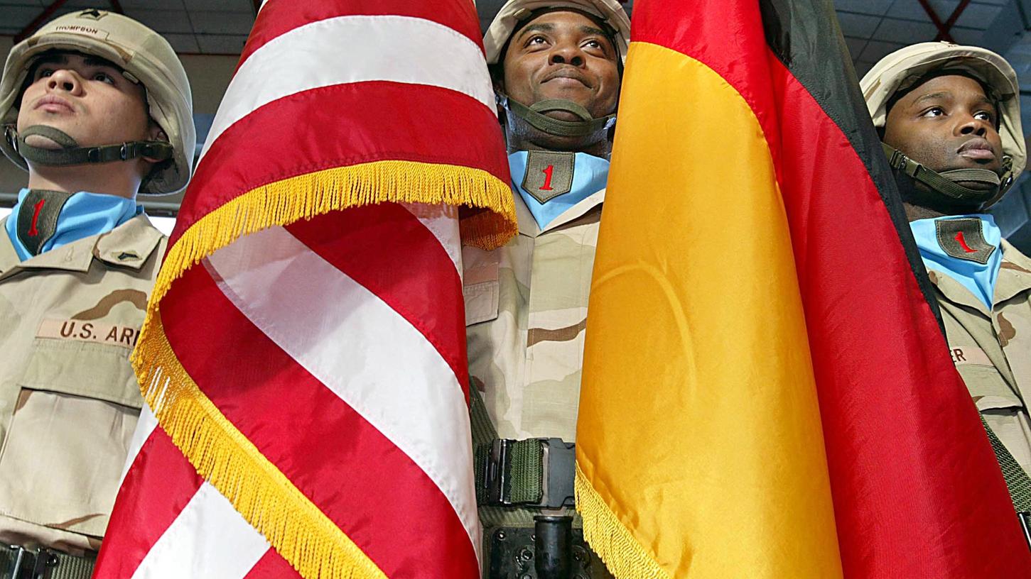 Drei Soldaten mit einer deutschen und einer US amerikanischen Flagge stehen bei der Verabschiedung der 1. US-Infanteriedivision am Hauptquartier in Würzburg. Der geplante Abzug von etwa einem Drittel der US-Soldaten aus Deutschland hat auch mehr als vier Monate nach der Ankündigung durch US-Präsident Trump noch nicht begonnen