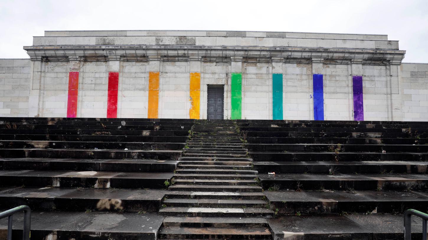 So bunt hat man den Nazibau noch nicht gesehen. Leider auch nicht lange. Schon gut einen Tag, nachdem ein anonymes Künstlerkollektiv die Steintribüne am Zeppelinfeld mit Regenbogenfarben bemalt hatte, ließ die Stadt diese wieder entfernen.