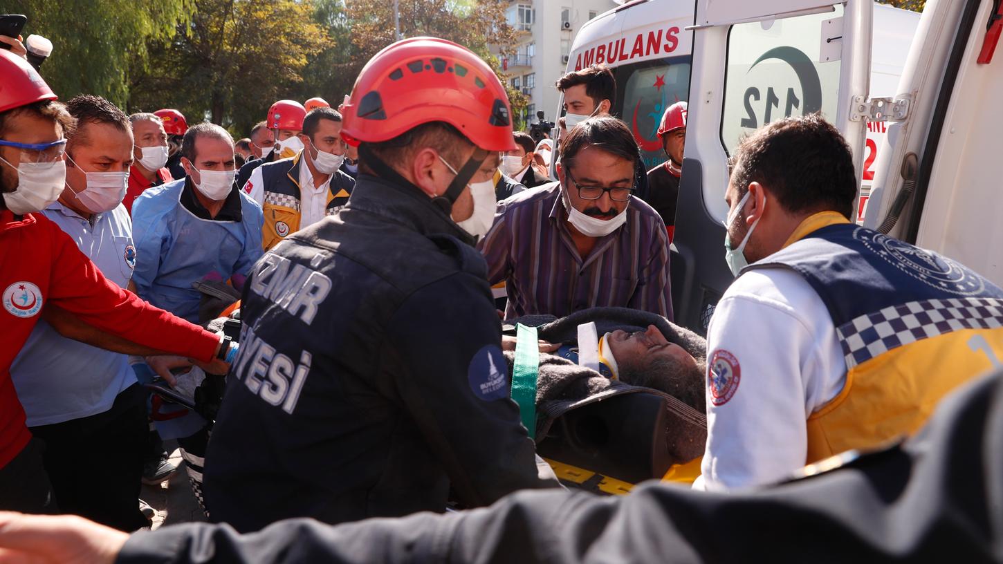 Sanitäter und Rettungskräfte tragen einen Verletzten aus den Trümmern eines eingestürzten Gebäudes zu einen Krankenwagen. 