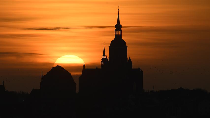 Orange ist beim Sonnenuntergang der Himmel über der Silhouette der Hansestadt Stralsund mit der Marienkirche, aufgenommen von der Insel Rügen aus. 