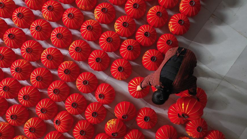 Eine Dorfbewohnerin hebt in China rote Laternen in die Höhe. 