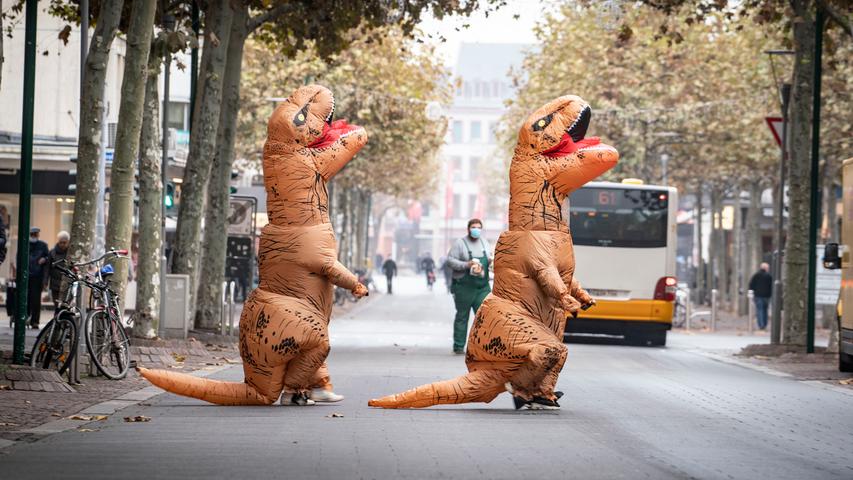 Zwei Karnevalistinnen in aufblasbaren Dinosaurier-Kostümen überqueren eine Straße nahe des Mainzer Schillerplatzes