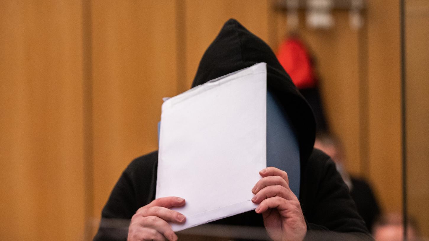 Ein Angeklagter versteckt sich in einem Gerichtssaal vor den Kameras der Presse.