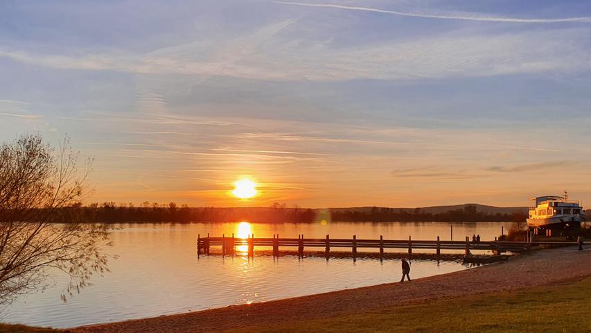 In rotgoldenes Licht taucht die untergehende Sonne den Altmühlsee im Seezentrum Muhr am See samt stegt und der sich in Winterruhe befindlichen MS Altmühlsee.