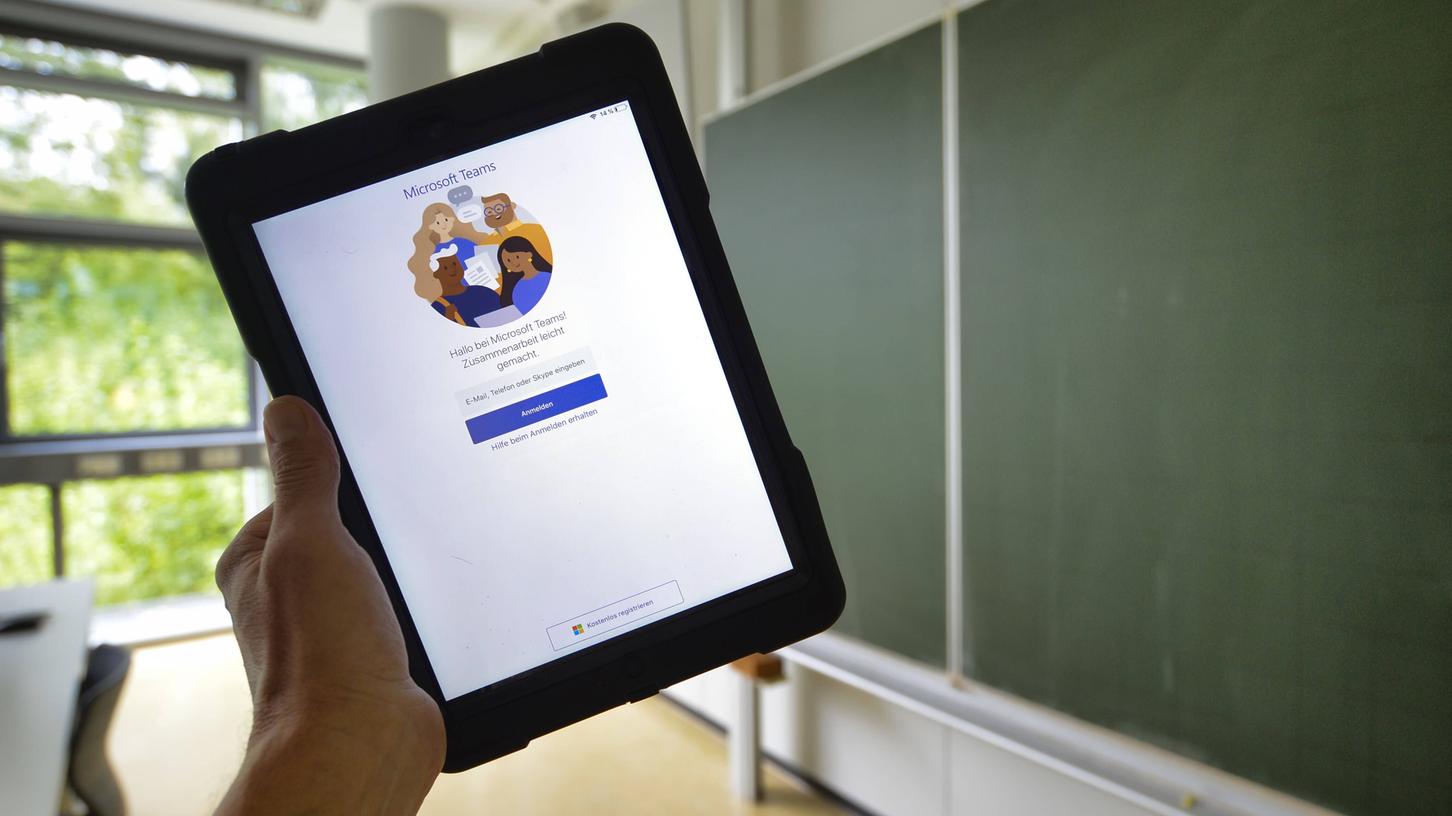 Ein Mann hält in einem Klassenzimmer ein iPad mit dem Logo von Microsoft Teams: In Zeiten des Lockdowns greifen viele Lehranstalten auf dieses Programm zurück, um homeschooling zu ermöglichen.

