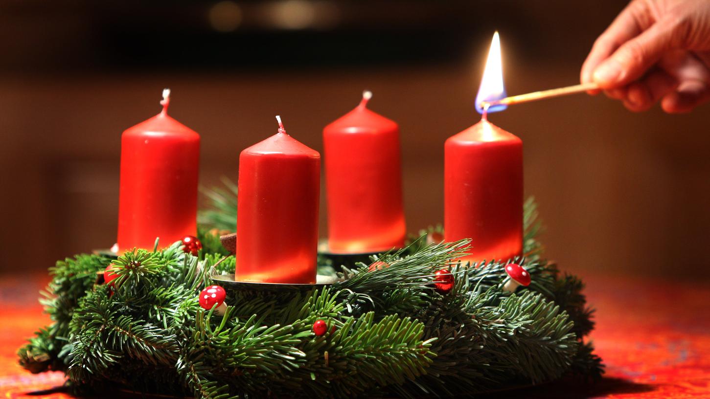 Eine Frau entzündet an einem selbst gebundenen Adventskranz eine Kerze. (Symbolbild) Eine Frau entzündet an einem selbst gebundenen Adventskranz eine Kerze. (Symbolbild)