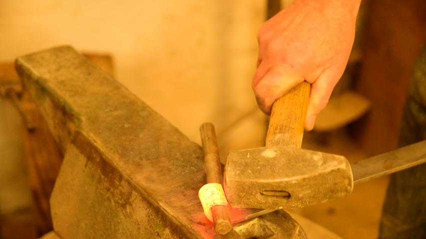In diesem Arbeitsschritt entsteht so etwa eine runde Öffnung, durch die man später ein anderes Eisenrohr hindurchschieben kann. Unter weiteren Hammerschlägen auf dem heißen Material werden die beiden Einzelteile dann endgültig ineinander verschlossen.