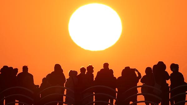 Menschen stehen am Strand und beobachten den letzten Sonnenuntergang im Jahr 2020.