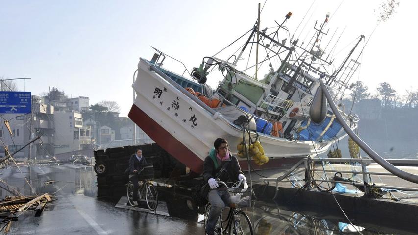 Vielerorts sahen sich die Helfer in 2011 Japan mit blanker Zerstörung konfrontiert. Das Ausmaß der Katastrophe wurde gerade dort deutlich, wo riesige Tsunami-Wellen ganze Ortschaften von der Landkarte radiert haben. Die Helfer versuchten Überlebende zu finden. Auf dem Bild sind zwei Fahrradfahrer zu sehen, die in der Stadt Kesennuma ein Schiff passieren, das durch den Tsunami aus dem Hafenbecken auf die Straße gehoben wurde.