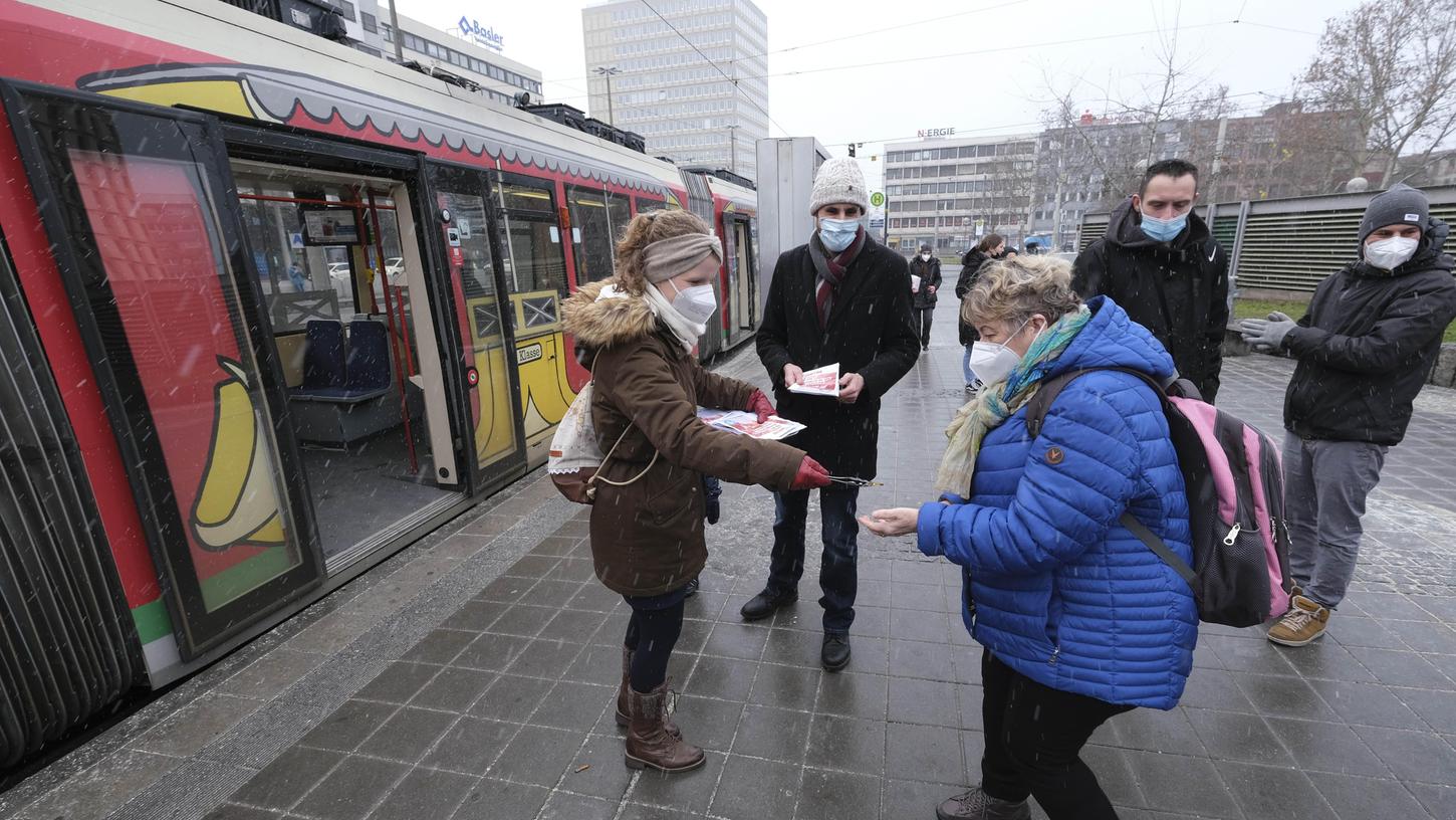 Die Linken-Stadträte Titus Schüller (Mitte) und Kathrin Flach Gomez verteilten kontaktlos per Zange und Tablett Schokoladentaler und Informationsblätter.  