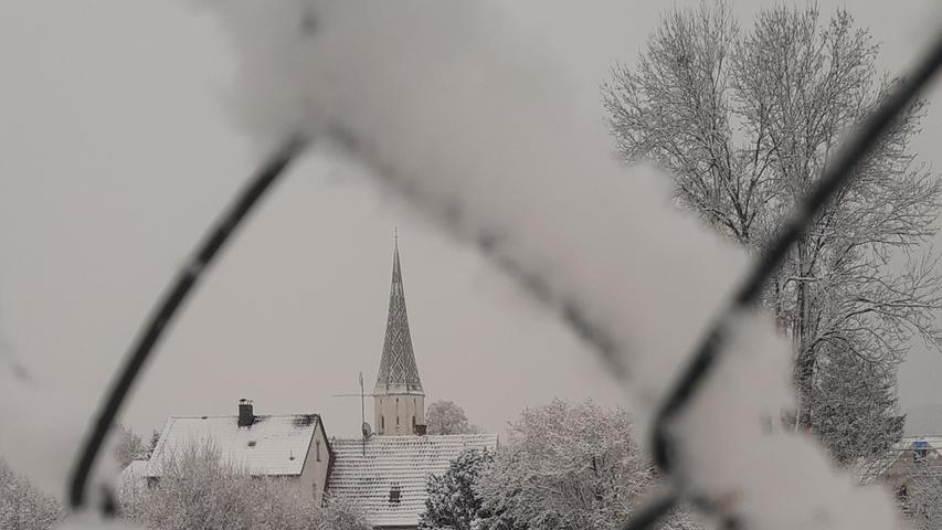 Die Meinheimer Kirche durch den schneebedeckten Maschendrahtzaun gesehen.