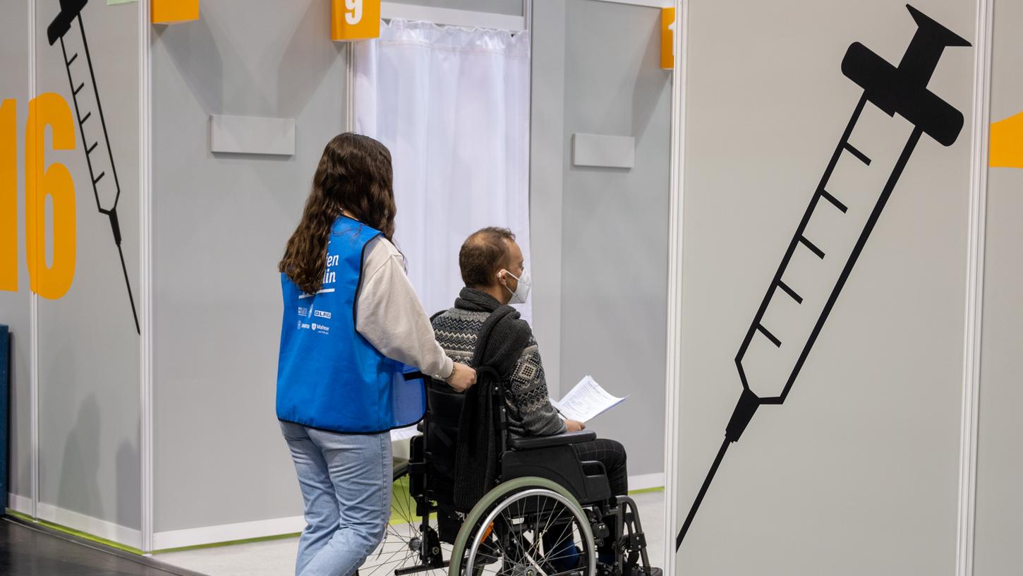 In einem Berliner Impfzentrum schiebt eine Helferin bei einem Probelauf einen Statisten im Rollstuhl durch die Hallen. Menschen mit Behinderung erhoffen sich, dass auch sie bald eine Corona-Impfung bekommen können.