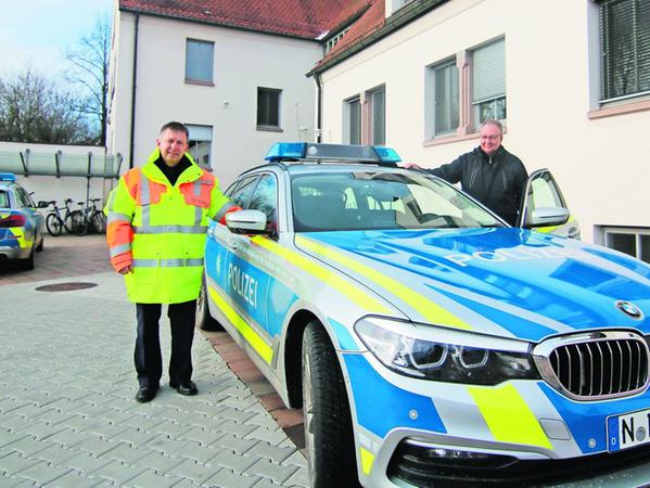 Die BMW-Kombis der Polizei Rothenburg haben mehr als 300 PS, Dienststellenleiter Stefan Schuster (links) zeigt einen der reflektierenden neongelben Schutzmäntel, rechts an der Tür steht Michael Zankl.
