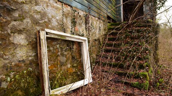 Wie bestellt und nicht abgeholt lehnt dieser Fensterrahmen an der Gebäudefassade. An ihm vorbei gelangt man über eine sehr unebene Treppe in den Innenbereich des Kellers. Die Dielen dort halten teilweise nicht mehr stand.