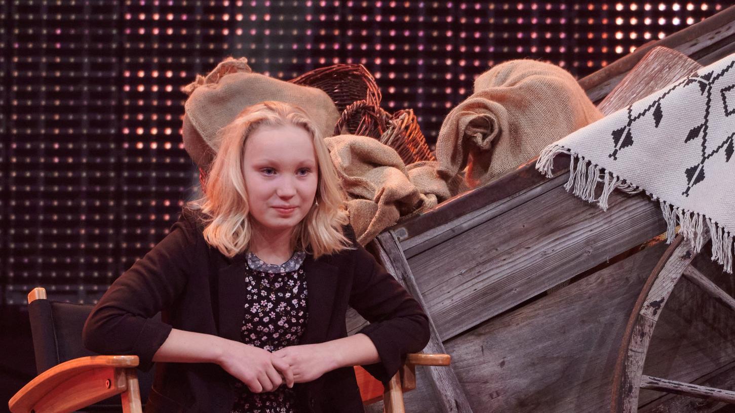 Die zwölfjährige Schauspielerin Helena Zengel sitzt vor einer Western Kulisse. 