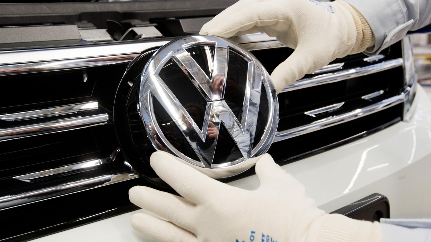 Ein Mitarbeiter montiert ein VW Logo an die Front eines VW Tiguan in der Endmontage im VW Werk