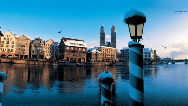 Wer Glück hat, kann bei gutem Wetter in Zürich einen solchen Anblick genießen. Hinter dem Limmat ragen die beiden Türme des Großmünsters in den Himmel über Zürich. Swiss International Airlines hebt mittlerweile ganzjährig in die Schweiz ab.