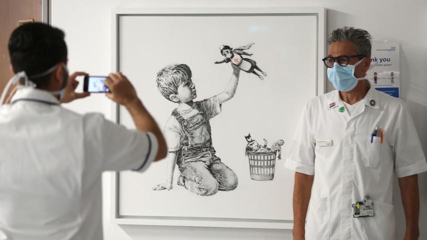 Ein Mitarbeiter lässt sich während des Lockdowns vor dem Werk "Game Changer" von Banksy, im Southampton General Hospital, fotografieren. Ein Werk des britischen Streetart-Künstlers Banksy ist am 23. März 2021 für 16,8 Millionen britische Pfund (19,5 Millionen Euro) in London versteigert worden.