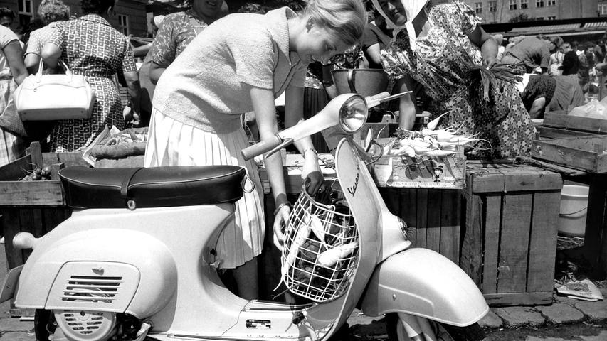 Eine Frau verstaut ihre Einkäufe in einem an ihrer Vespa angebrachten Korb, aufgenommen 1964. Die erste Vespa kam 1946 in Italien auf den Markt.