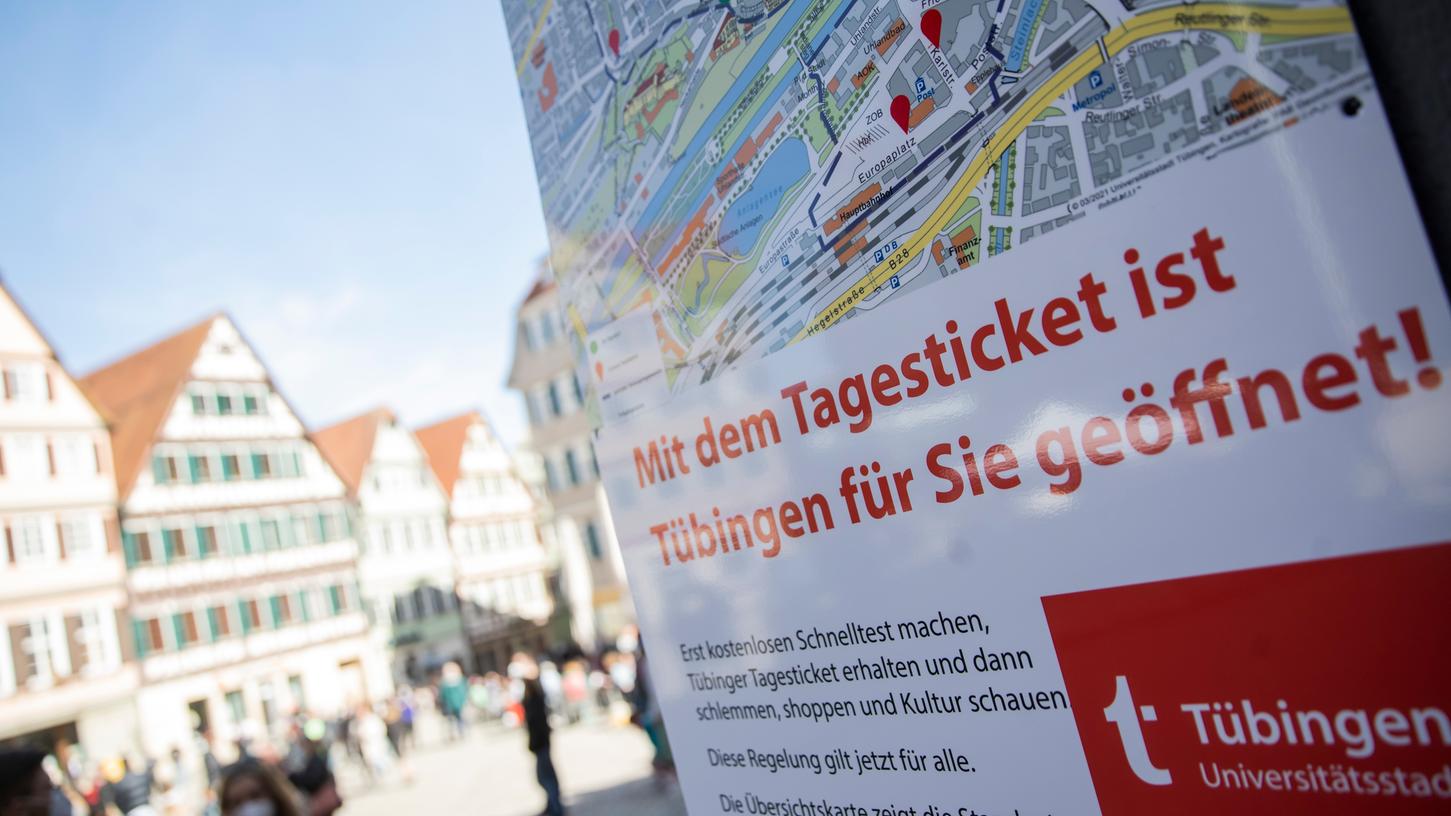  Auf dem Tübinger Rathausplatz hängt ein Schild mit der Aufschrift «Mit dem Tagesticket ist Tübingen für Sie geöffnet!». In Tübingen können Menschen in der Stadt kostenlose Corona-Tests machen. Mit einem negativen Testergebnis können die getesteten Personen zum Beispiel in Modeläden einkaufen oder zum Friseur.